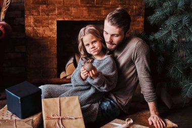 Sevimli küçük kız babasıyla bir yerde otururken Noel top tutan hediyeler tarafından çevrili mutluluk