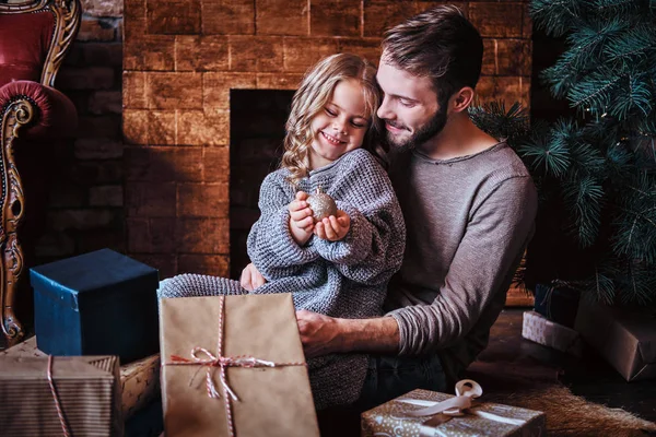 Hediyeler, şömine ve Noel ağacı yanında sevimli küçük kız babasıyla bir yerde otururken Noel top tutan çevrili mutluluk