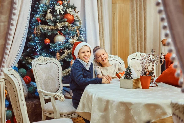 Sister and brother sitting at the table in an elegant living room decorated for Christmas. — Stock Photo, Image