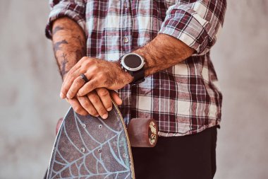 Bir kaykay üzerinde yaslanmış bir kareli gömlek giyen bir adam kısmi görünümünü. Gri bir arka plan üzerinde izole.