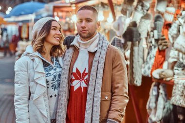 Noel zamanda sokakta yürüyen genç romantik bir çift ayakta yakınındaki dükkanlar akşam, birlikte vakit zevk dekore.