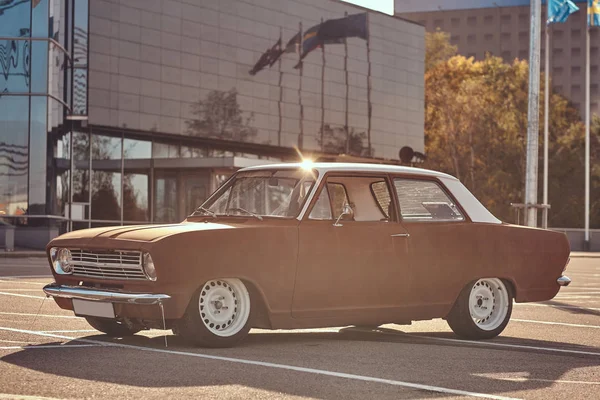 Tuned old retro car with country style in the city parking near skyscraper at bright sunset.