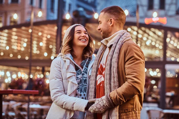 Ein junges romantisches Paar, das sich an den Händen hält und einander ansieht, während es zur Weihnachtszeit auf der Straße steht und die gemeinsame Zeit genießt. — Stockfoto