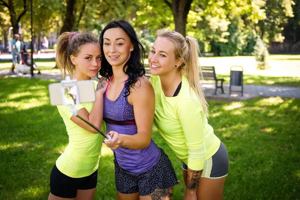 Üç sportif kadın park açık havada adlı arkadaş selfie bir sopa ile bir cep telefonu üzerinde gülümseyen. — Stok fotoğraf