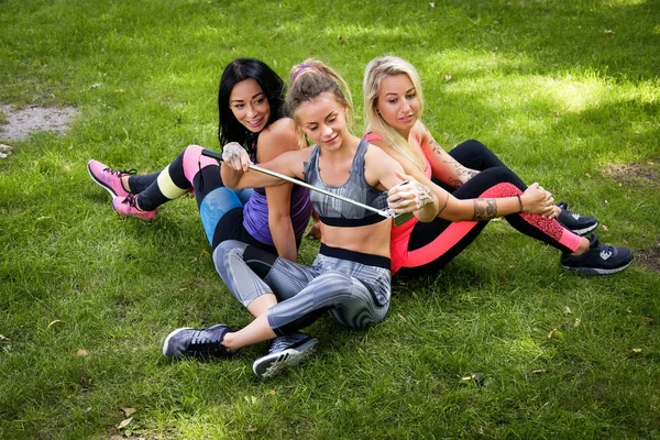 Három sportos női meg ül a fűben, a park a szabadban, hogy selfie egy telefont, egy bottal — Stock Fotó