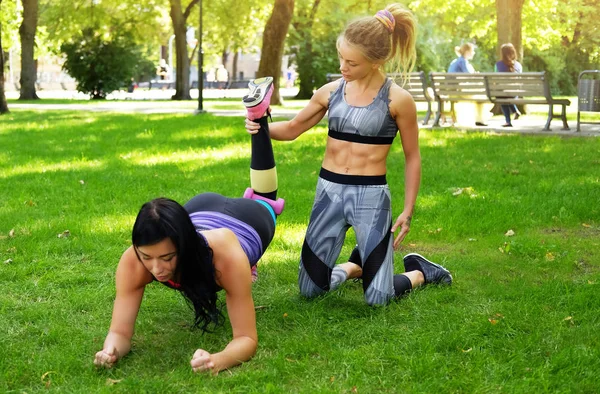 Allenamento al parco all'aperto, ragazza con il suo allenatore facendo esercizi sull'erba . — Foto Stock