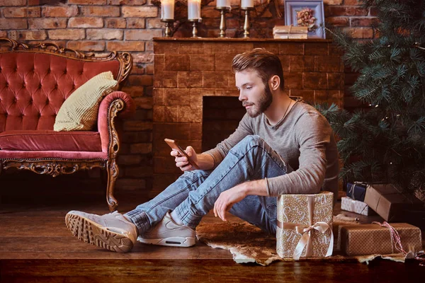 一个年轻的帅哥坐在被礼物包围的地板上和朋友通电话 — 图库照片