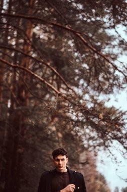 Omuzlarını sonbahar ormandaki kapsayan montlu genç adam.