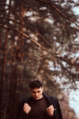 Omuzlarını sonbahar ormandaki kapsayan montlu genç adam.