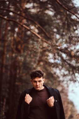 Omuzlarını sonbahar ormandaki kapsayan montlu genç adam.