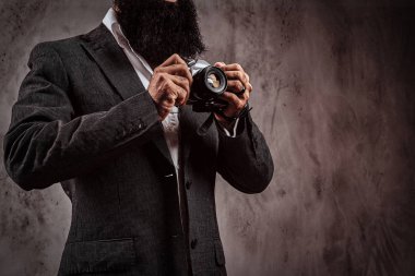 Bir kamera tutarak resmi takım elbise giymiş bir sakallı erkek resim kırpılmış.