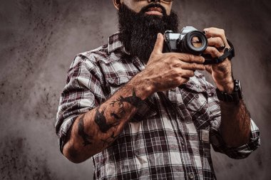 Resim dövmeli bir sakallı erkek bir kamera tutarak bir kareli gömlek giyen kırpılmış.