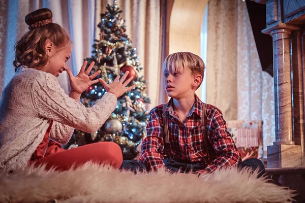 Happy brother and sister having fun while sitting on a fur carpet near a Christmas tree at home. — Stock Photo, Image