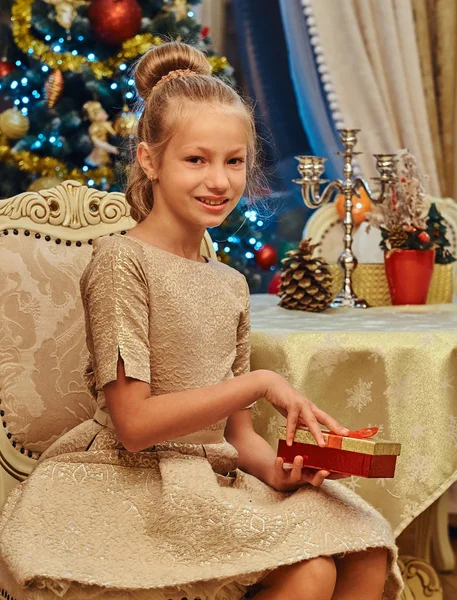 Девушка в красивом платье сидит на стуле и открывает подарочную коробку — стоковое фото