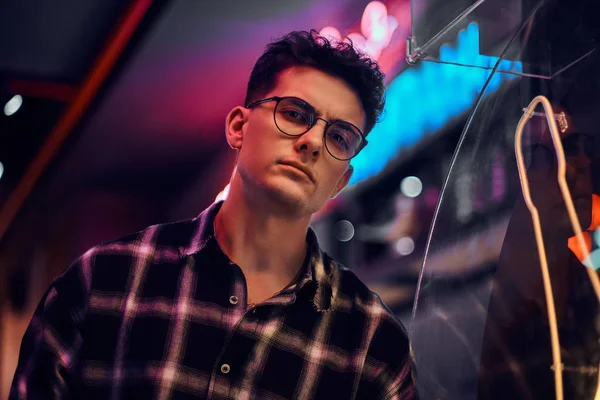 Un joven guapo de pie por la noche en la calle. Letreros iluminados, neón, luces . — Foto de Stock