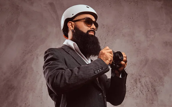 Arabe barbu mâle portant une combinaison formelle lunettes de soleil et casque de skate faire une photo avec appareil photo . — Photo