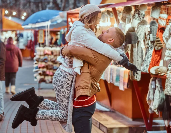 Jovem casal romântico gostando de passar o tempo juntos no Natal na rua perto de lojas decoradas. Jovem feliz levantou sua namorada . — Fotografia de Stock