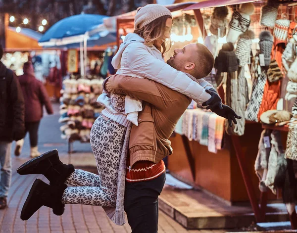 Молода романтична пара насолоджується проведенням часу разом на Різдво на вулиці біля прикрашених магазинів. Щасливий молодий хлопець виховав свою дівчину . — стокове фото