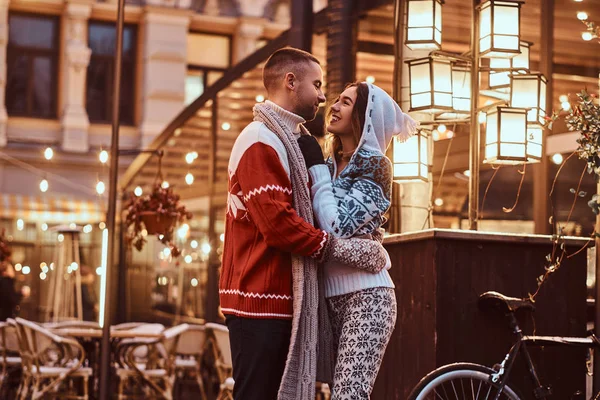 Um jovem casal romântico vestindo roupas quentes abraçando ao ar livre na rua à noite na época do Natal, gostando de passar o tempo juntos . — Fotografia de Stock