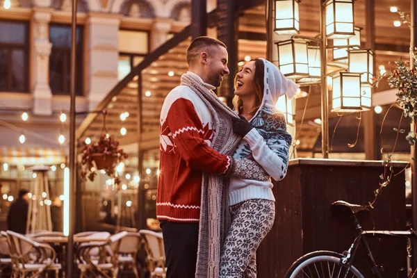 Um jovem casal romântico vestindo roupas quentes abraçando ao ar livre na rua à noite na época do Natal, gostando de passar o tempo juntos . — Fotografia de Stock