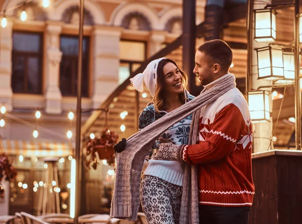 Una joven pareja romántica con ropa abrigada abrazándose al aire libre en la calle de la noche en Navidad, disfrutando pasar tiempo juntos . — Foto de Stock