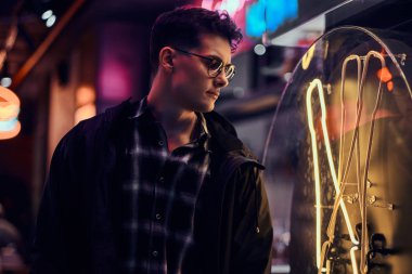 Geceleri sokakta ışıklı tabela bakarak dalgın bir genç adam.