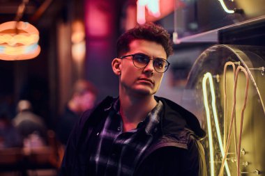 Gece sokakta duran yakışıklı bir genç adam. Işıklı tabela, neon, ışıklar.