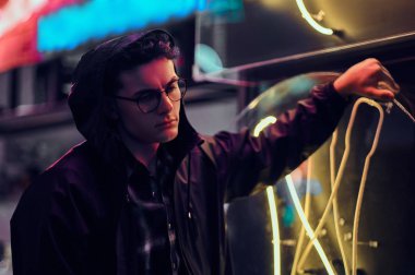 Dalgın bir genç adam sokakta bir ışıklı tabela üzerinde geceleri yaslanmış.