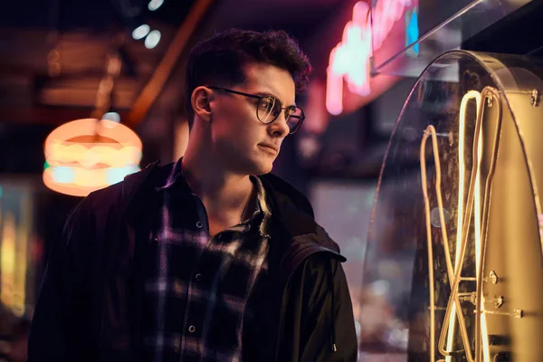 Un joven pensativo mirando el letrero iluminado en la calle por la noche . — Foto de Stock