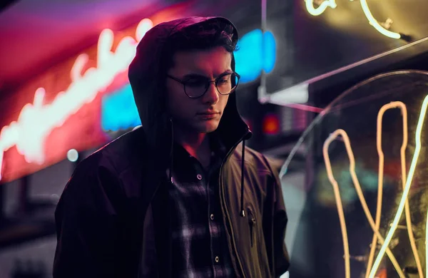 Przystojny młody mężczyzna stojący w nocy na ulicy. Podświetlane szyldy, neon, światła. — Zdjęcie stockowe