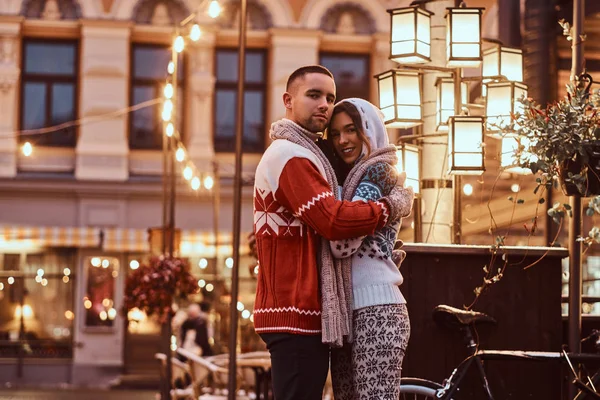 Una giovane coppia romantica indossa vestiti caldi che si abbracciano all'aperto in strada la sera a Natale, godendo di trascorrere del tempo insieme . — Foto Stock