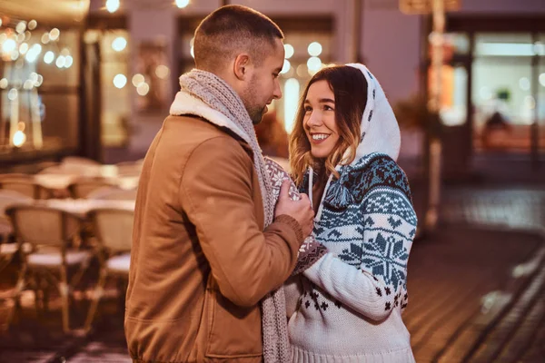 Um jovem casal romântico vestindo roupas quentes de mãos dadas e aquecendo enquanto estava em pé na rua à noite na época do Natal, desfrutando de passar o tempo juntos . — Fotografia de Stock