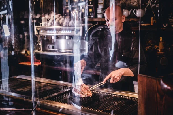 Kock Matlagning läckra nötstek på ett kök, står bakom skyddande glas i en restaurang. — Stockfoto