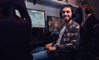 Oyun bir sandalyede oturan ve bir kamera bir oyun kulüp veya internet kafede bakarak bir asker gömleği giyen genç neşeli Hint adam.