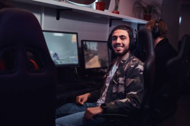 Oyun bir sandalyede oturan ve bir kamera bir oyun kulüp veya internet kafede bakarak bir asker gömleği giyen genç neşeli Hint adam.