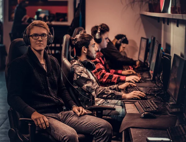 Un giovane giocatore intelligente che indossa un maglione e occhiali seduto su una sedia giocatore e guardando una fotocamera in un club di gioco o internet cafè . — Foto Stock