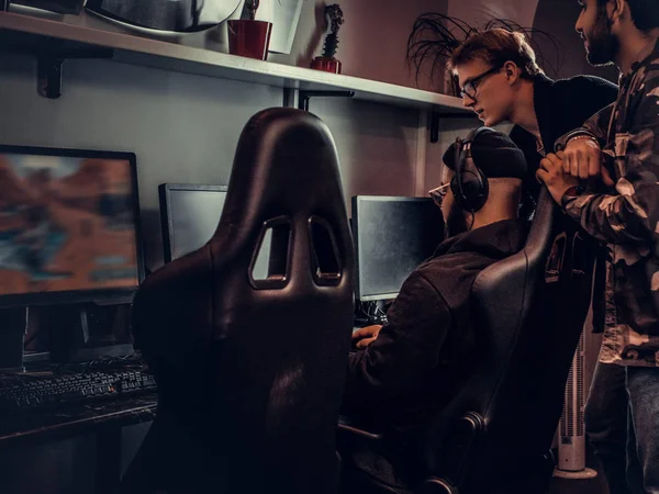 Zwei Jungs beobachten ihren Freund beim Spielen von Videospielen in einem Spielclub oder Internetcafé. — Stockfoto