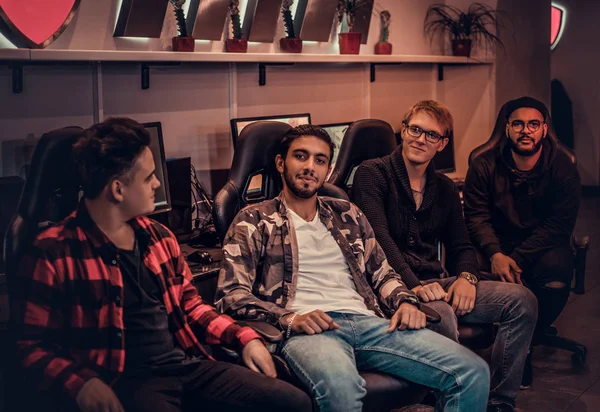 A team of multiracial teenage gamers sitting on gamer chairs and looking at a camera in a gaming club or internet cafe. — Stock Photo, Image