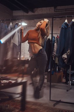 Çıplak bir göbek ve açılarak pantolon bir giyim mağazası montaj odasında giysileri ile bir raf üzerinde yaslanmış yorgun bir kızla.