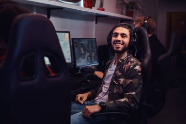 Oyun bir sandalyede oturan ve bir kamera bir oyun kulüp veya internet kafede bakarak bir asker gömleği giyen genç neşeli Hint adam.