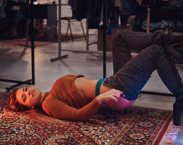Une belle fille tirant séduisamment vers le haut pantalon tout en étant couché sur le sol dans la salle d'essayage d'un magasin de vêtements . — Photo