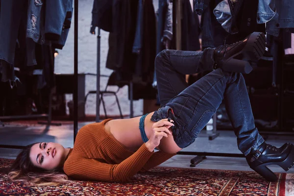 Uma garota sexy sedutoramente puxando as calças enquanto estava deitada no chão no provador de uma loja de roupas . — Fotografia de Stock