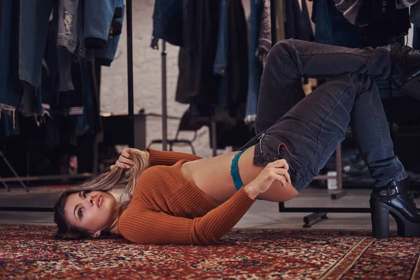 Сексуальна дівчина спокусливо підтягує штани, лежачи на підлозі в примірювальній кімнаті магазину одягу . — стокове фото