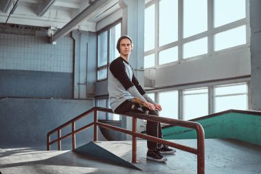 Gömlek ve holding onun yönetim kurulu skatepark kapalı bir eziyet demiryolu üzerinde otururken şapka giyen genç yakışıklı adam