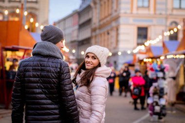 Noel Fuarı ile akşam sokakta yürürken kış giysileri giyen genç bir romantik çift