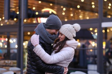 Birlikte Noel zamanı dışında bir kafe yakınındaki akşam sokakta sarılma sıcak giysiler giyen genç bir romantik çift