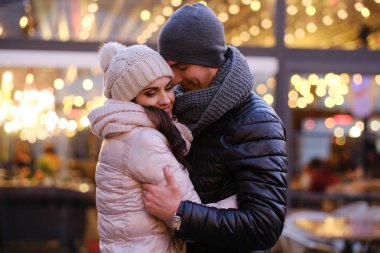 Birlikte Noel zamanı dışında bir kafe yakınındaki akşam sokakta sarılma sıcak giysiler giyen genç bir romantik çift