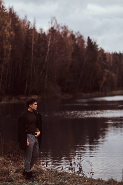 Yakışıklı bir genç adam yakın bir göl sonbahar ormandaki ayakta.