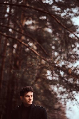 Sonbahar ormanda siyah bir ceket giyen genç adam.
