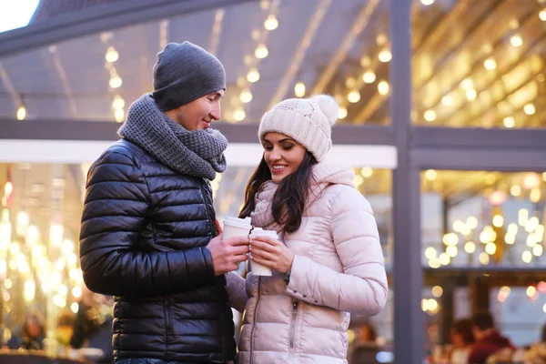 Happy romantic couple wearing warm clothes enjoying spending time together on a date in evening street near a cafe outside at Christmas time